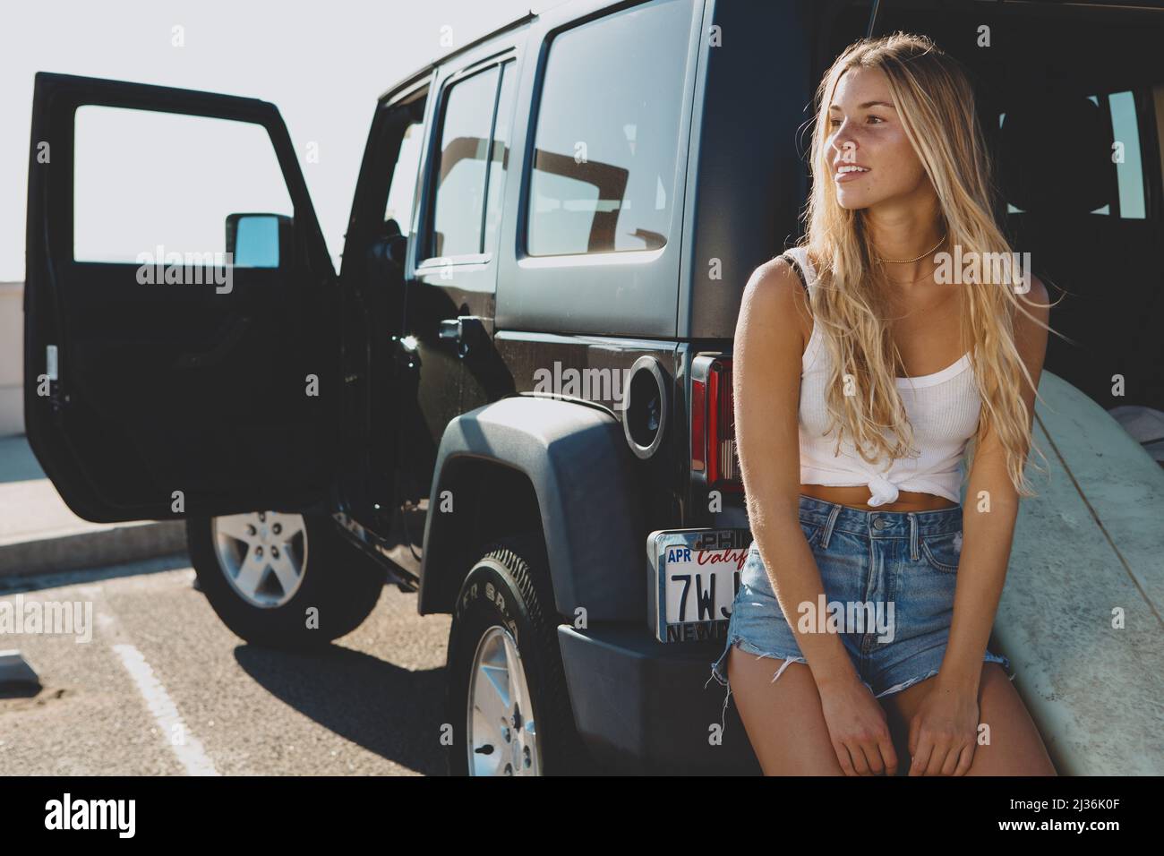 surfer girl sitting at a car with surfboard. On film California Stock Photo