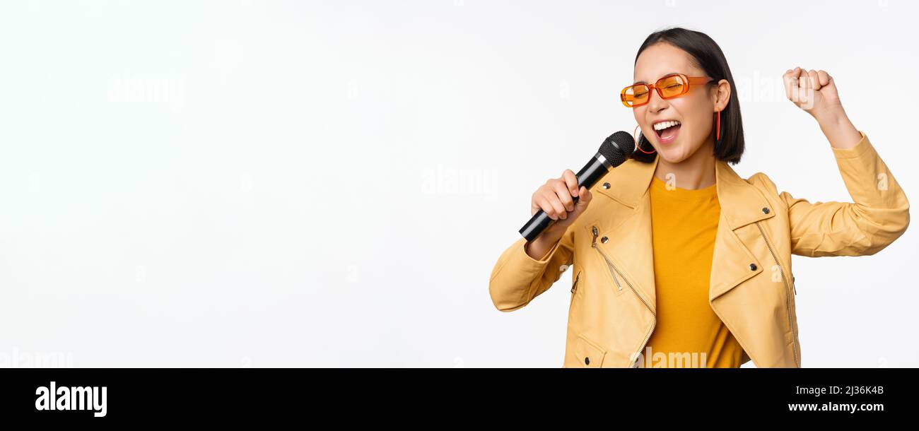 Stylish asian girl in sunglasses, singing songs with microphone ...