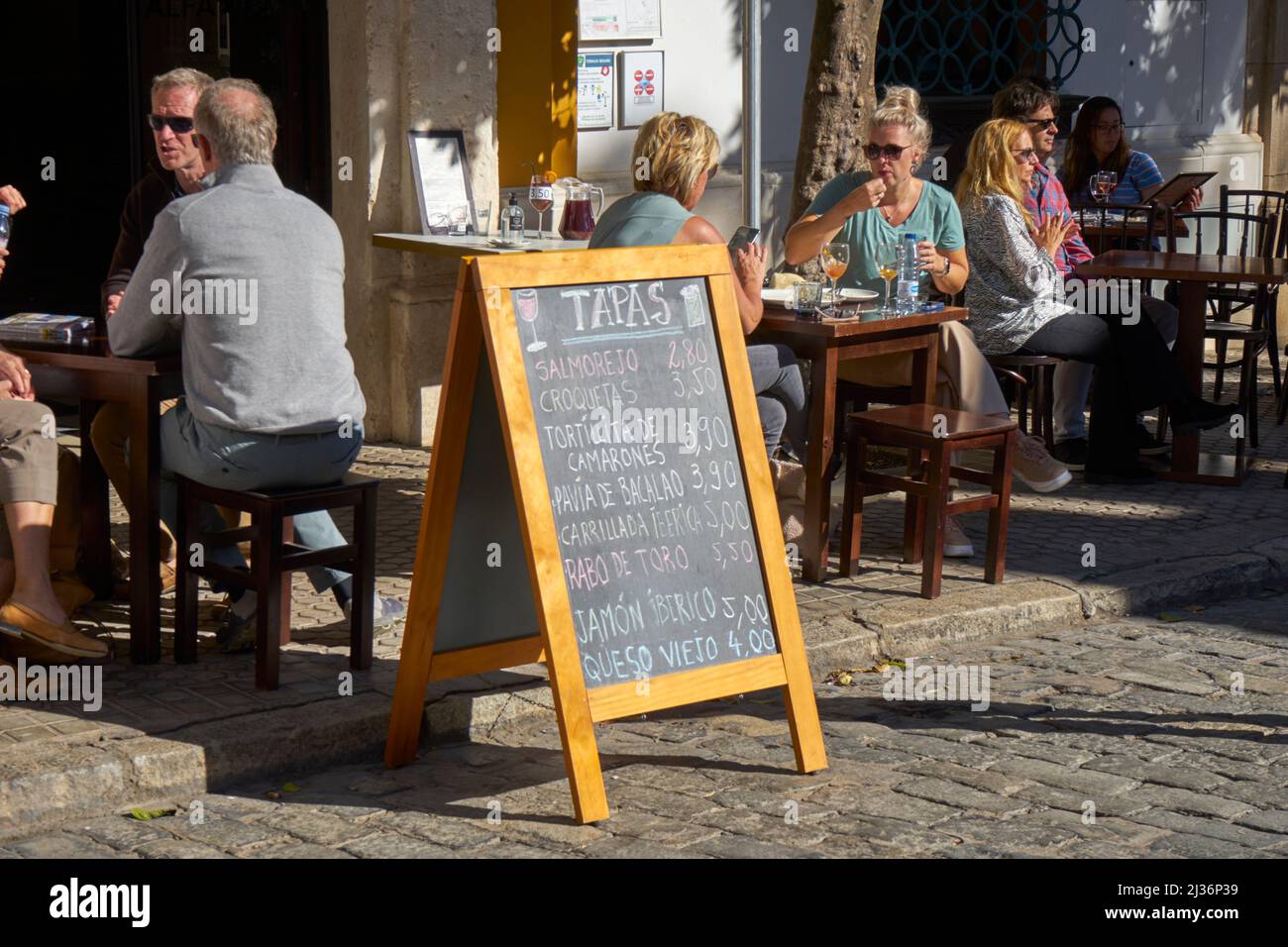 Al fresco tapas bar in sunshine with tourists and large tapas menu, Seville, Spain Stock Photo