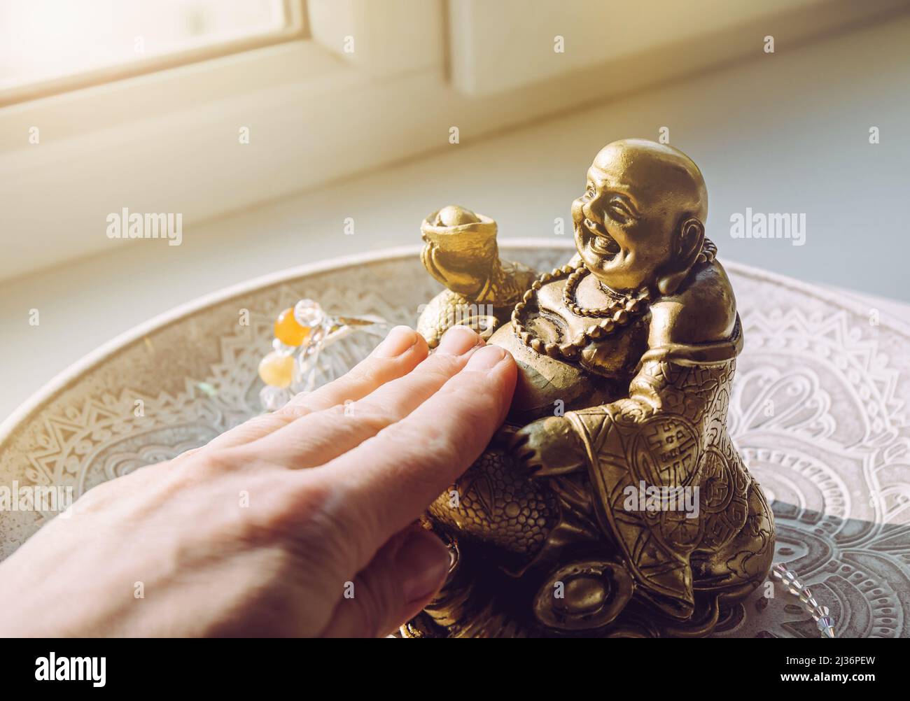 Person hand rubbing small golden laughing Buddha figurine tummy. It