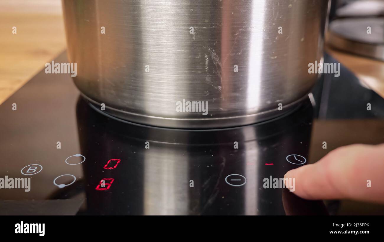 Man puts saucepan and turns on electric induction cooker Stock Photo