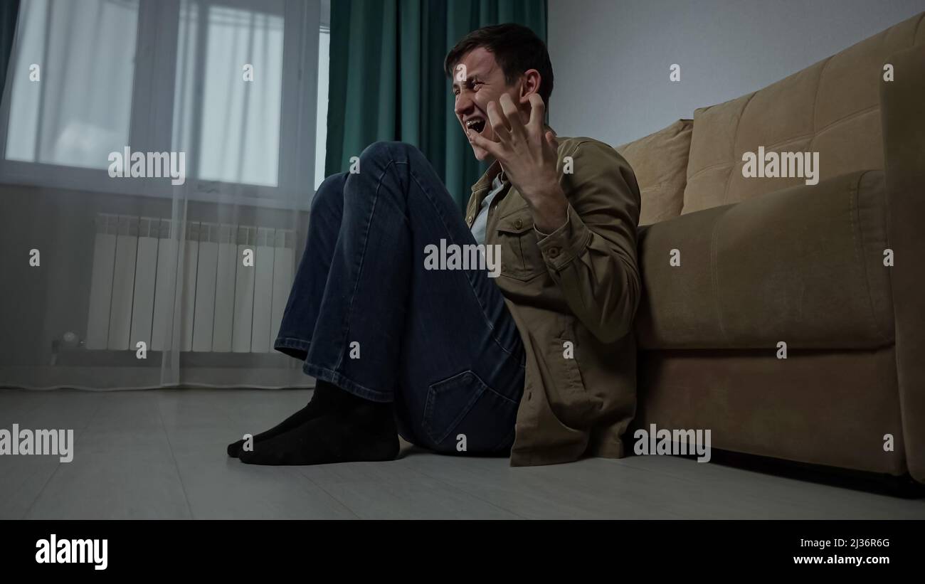 Depressed sad man with hugging the knees sits on floor near sofa in ...