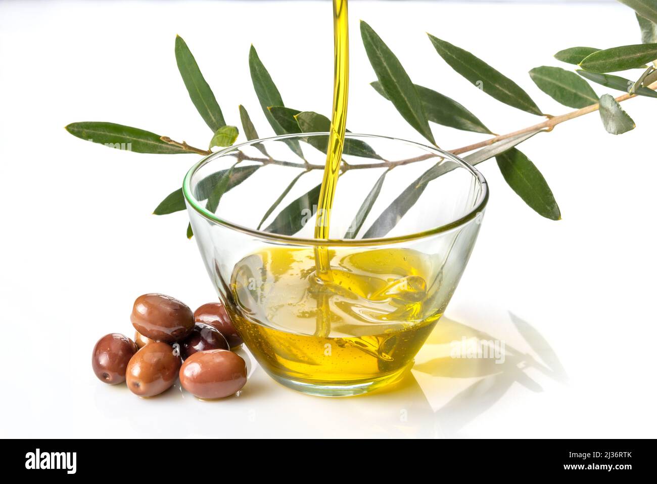 Olive oil pouring into glass bowl with olives and branch with olive leaves isolated on white Stock Photo