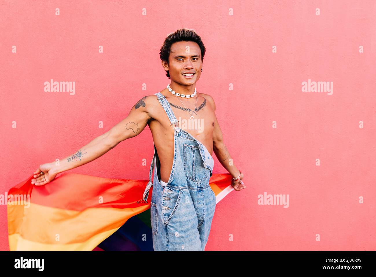 Young guy in denim overalls holding a rainbow flag outdoors Stock Photo