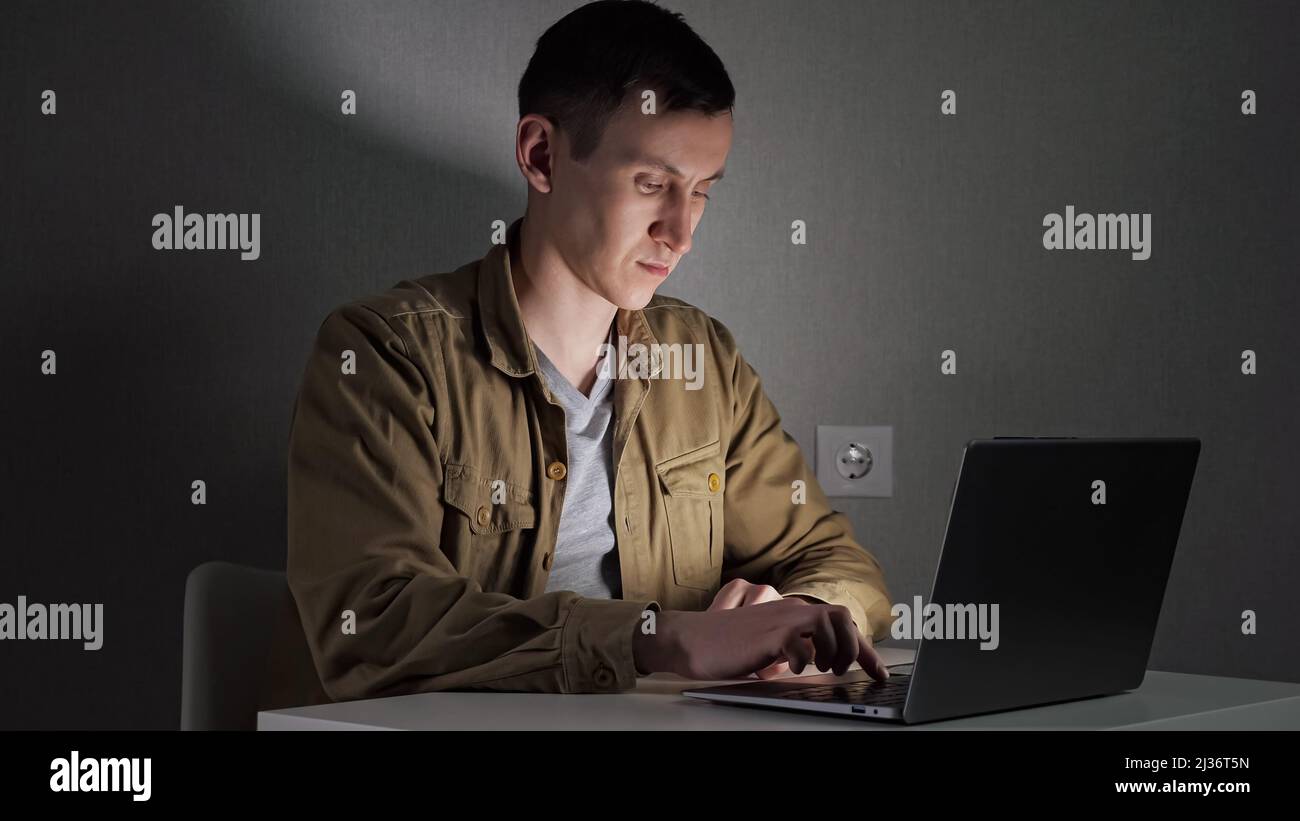Young man freelancer works at night typing text on laptop Stock Photo