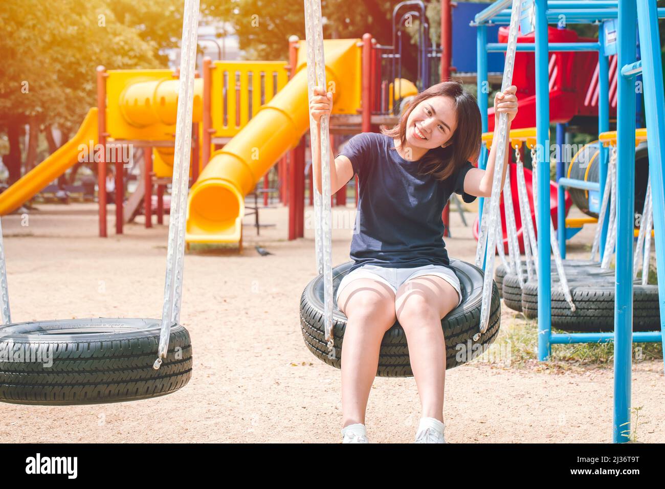 Asian cute teen happy smile sitting at swing kid playground park, leisure young innocent girl. Stock Photo