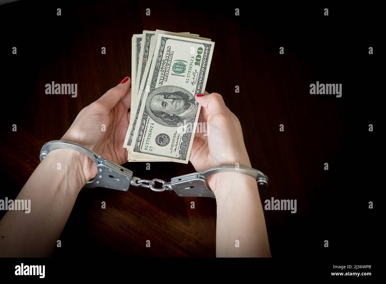 women's handcuffed hands hold dollars on a dark wooden background Stock Photo
