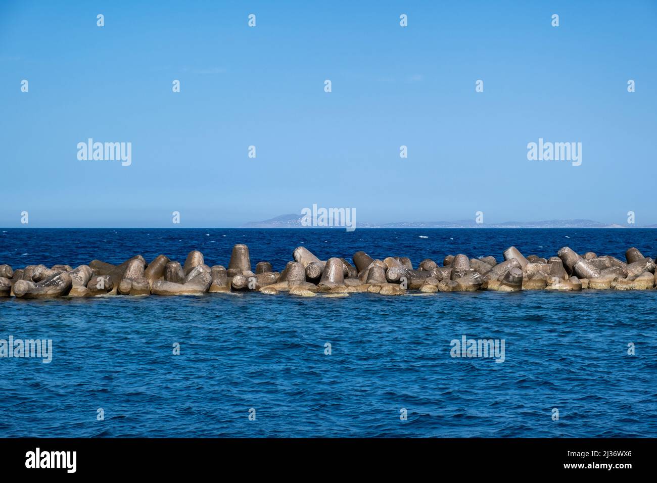 Breakwater concrete block, Sea rocky wall for sea storm protection in Aegean water, clear blue sky background. Ermoupolis port, Syros island, Greece. Stock Photo