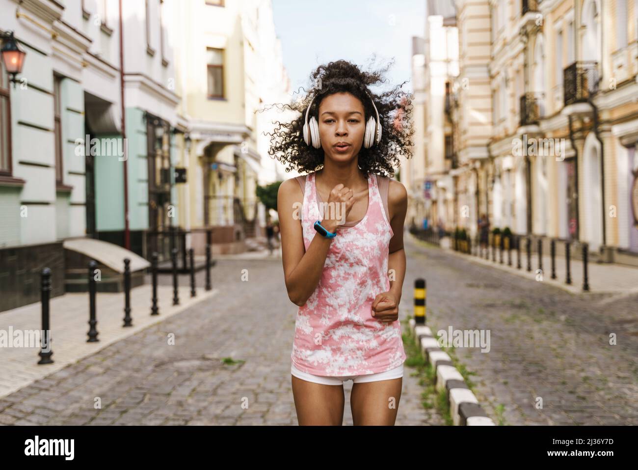 Young black woman listening music with headphones while running on city