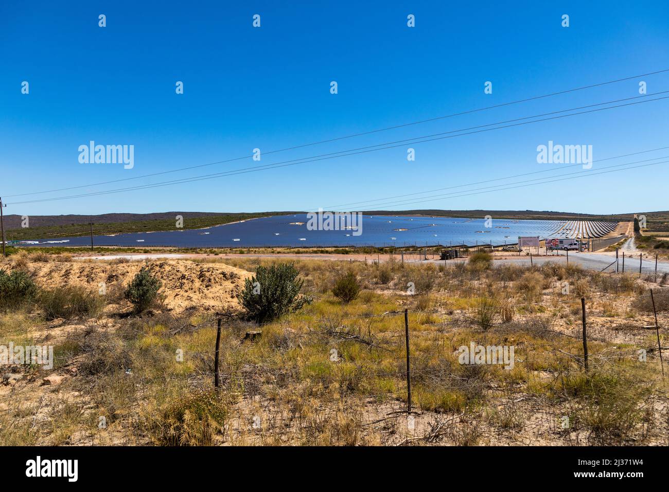 Large solar farm in a remote semi desert area, with paralel rows of photovoltaic panels. no clouds in the sky Stock Photo