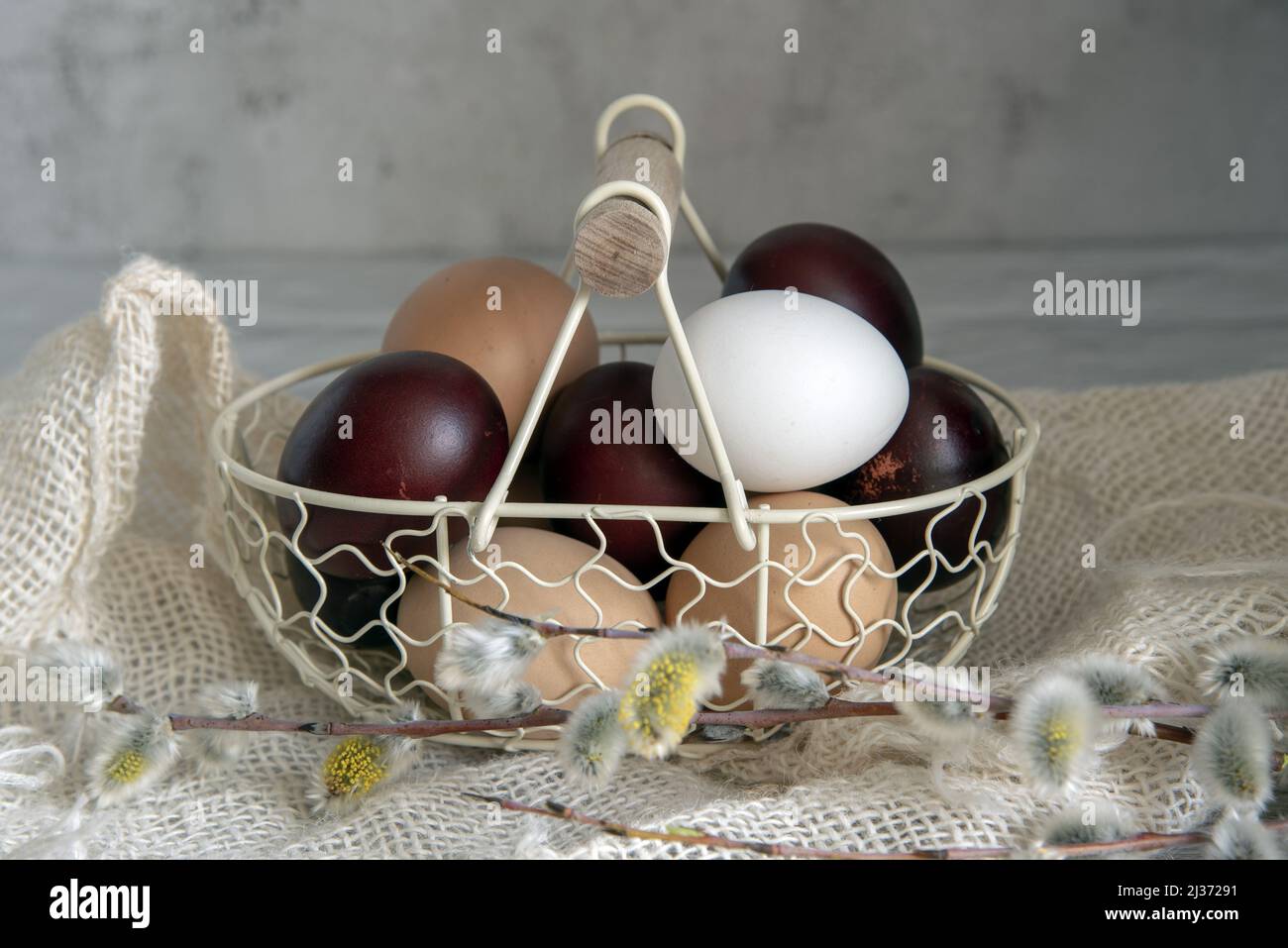 Easter colored eggs and natural eggs lie in a small basket decorated ...