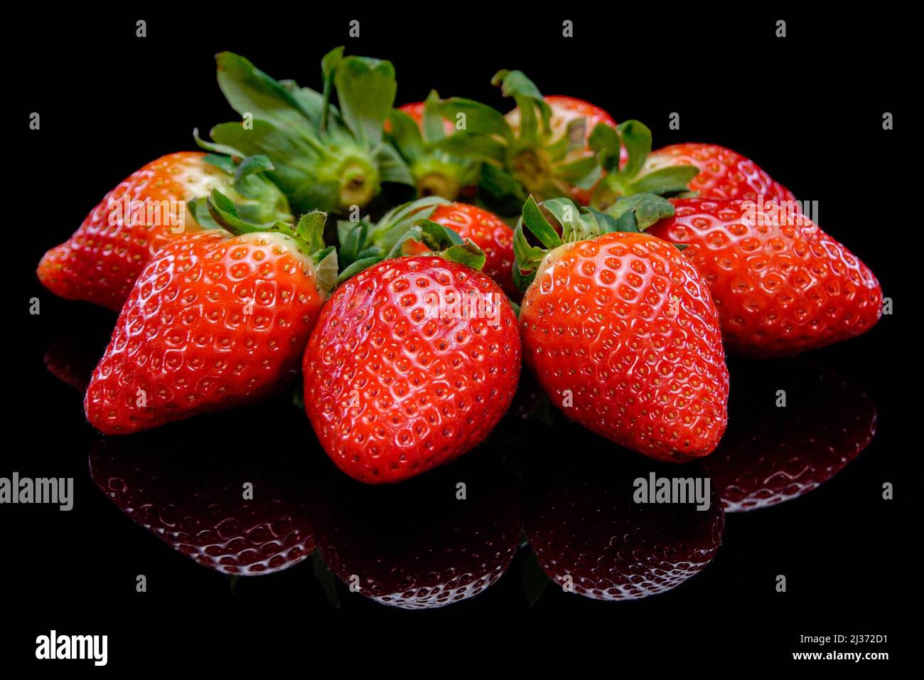 Strawberries on a black background close up view. Fresh, organic vibrant red strawberry. Raw vegan summer snack. Stock Photo