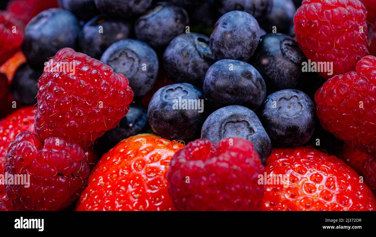Strawberries, raspberries and blueberries on a black background. Fresh, organic vibrant summer berries, close up view.  Raw vegan summer snack. Stock Photo