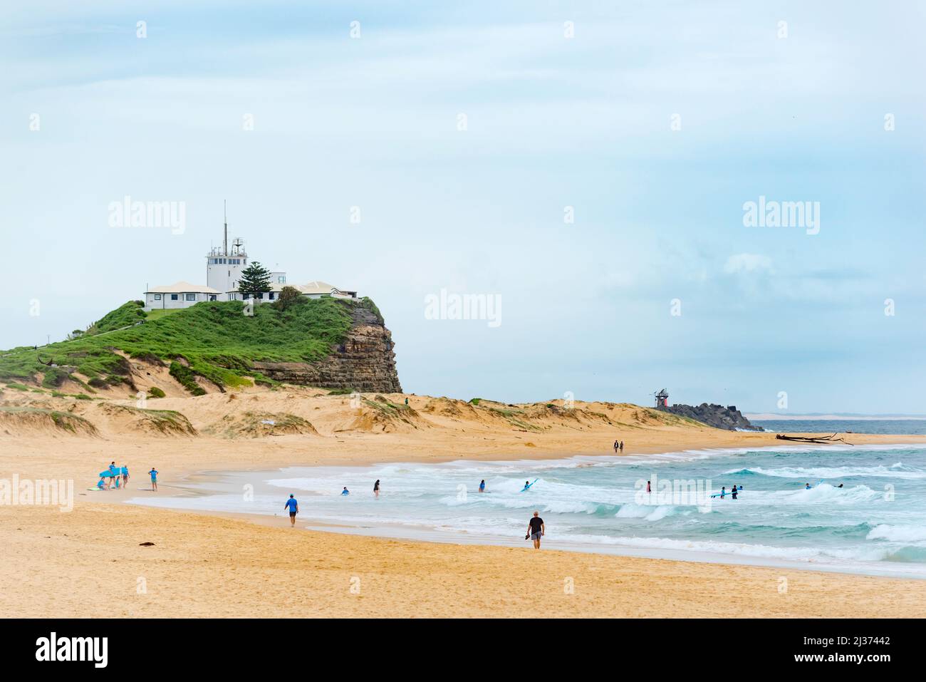 People swimming and walking on Nobbys Beach, Newcastle, Australia below the still active Nobbys Lighthouse that was originally constructed in 1846 Stock Photo