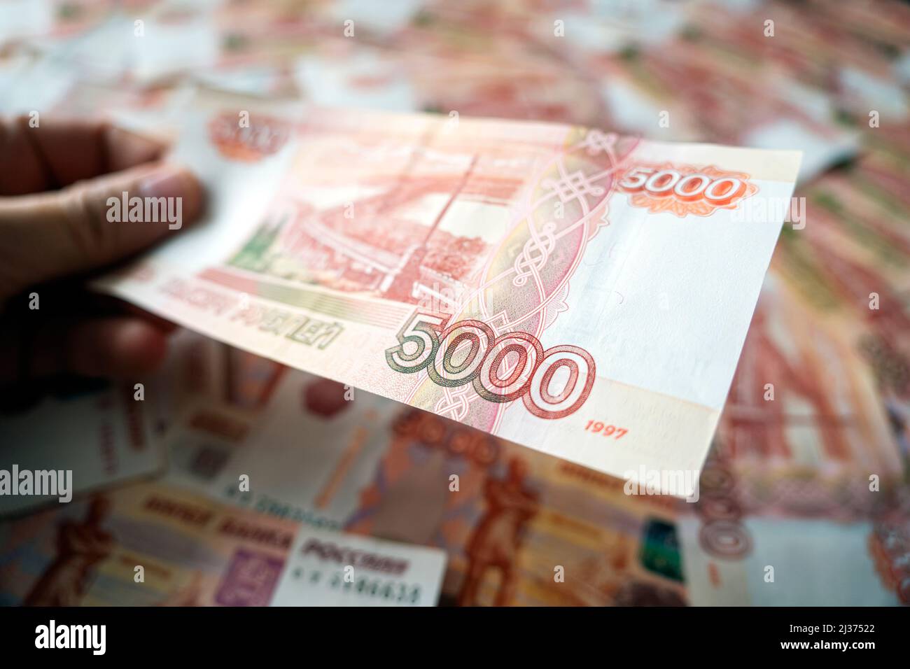 a lot of money in hand of a young businessman on a blue background. A stack of banknotes of Russian rubles with a face value of 5000 rubles. successfu Stock Photo