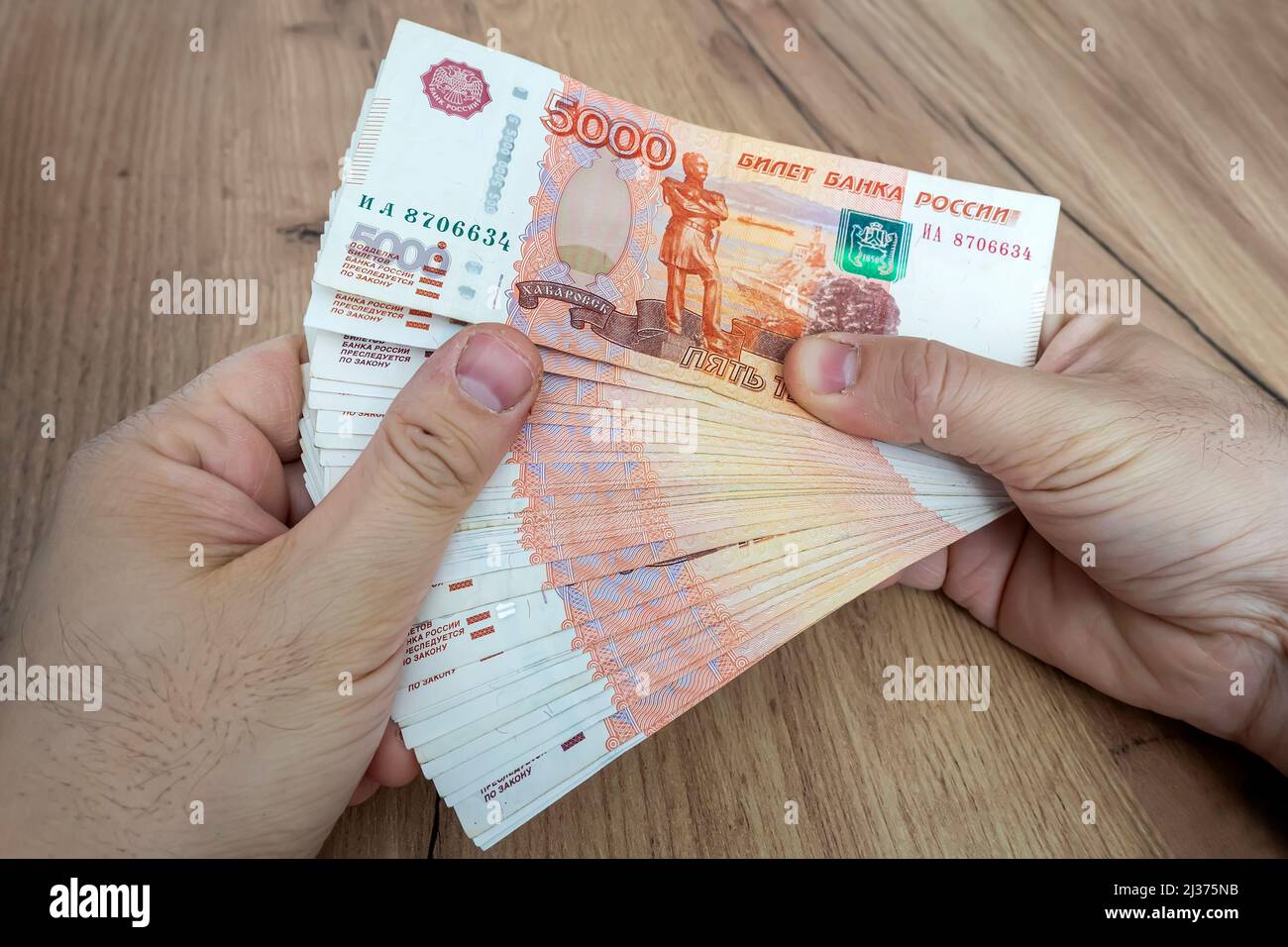 a lot of money in the hand of a young businessman on a blue background. stack of banknotes of Russian rubles with a face value of 5000 rubles. success Stock Photo