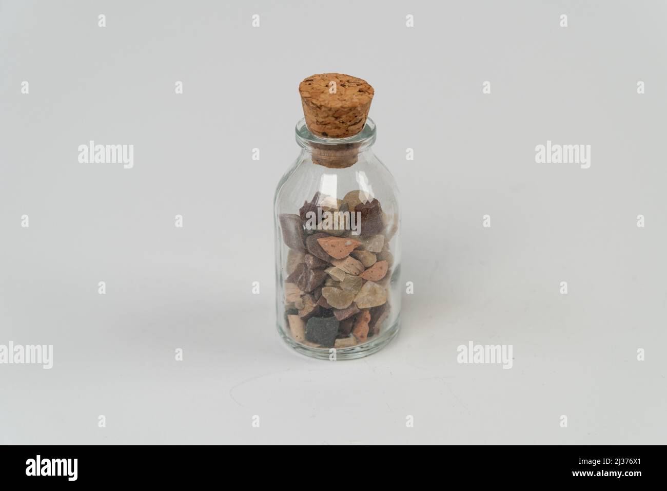 Small rocks in glass bottle with cork stopper isolated on white background, for remembrance, broken sand stones in glass bottle, saving memory on jar, Stock Photo
