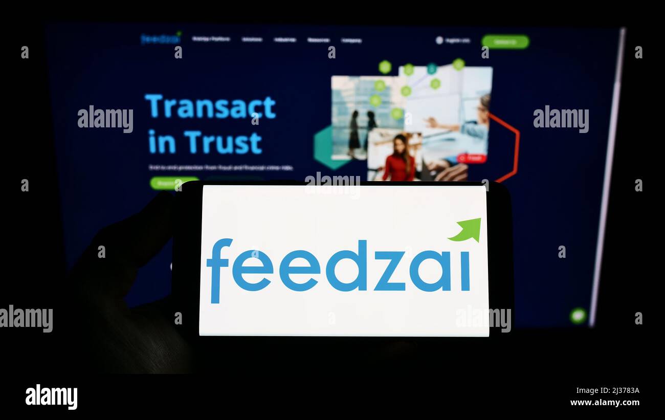 Person holding smartphone with logo of Portuguese risk management company Feedzai on screen in front of website. Focus on phone display. Stock Photo