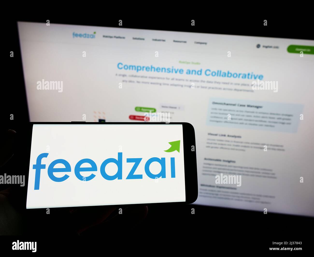 Person holding mobile phone with logo of Portuguese risk management company Feedzai on screen in front of web page. Focus on phone display. Stock Photo