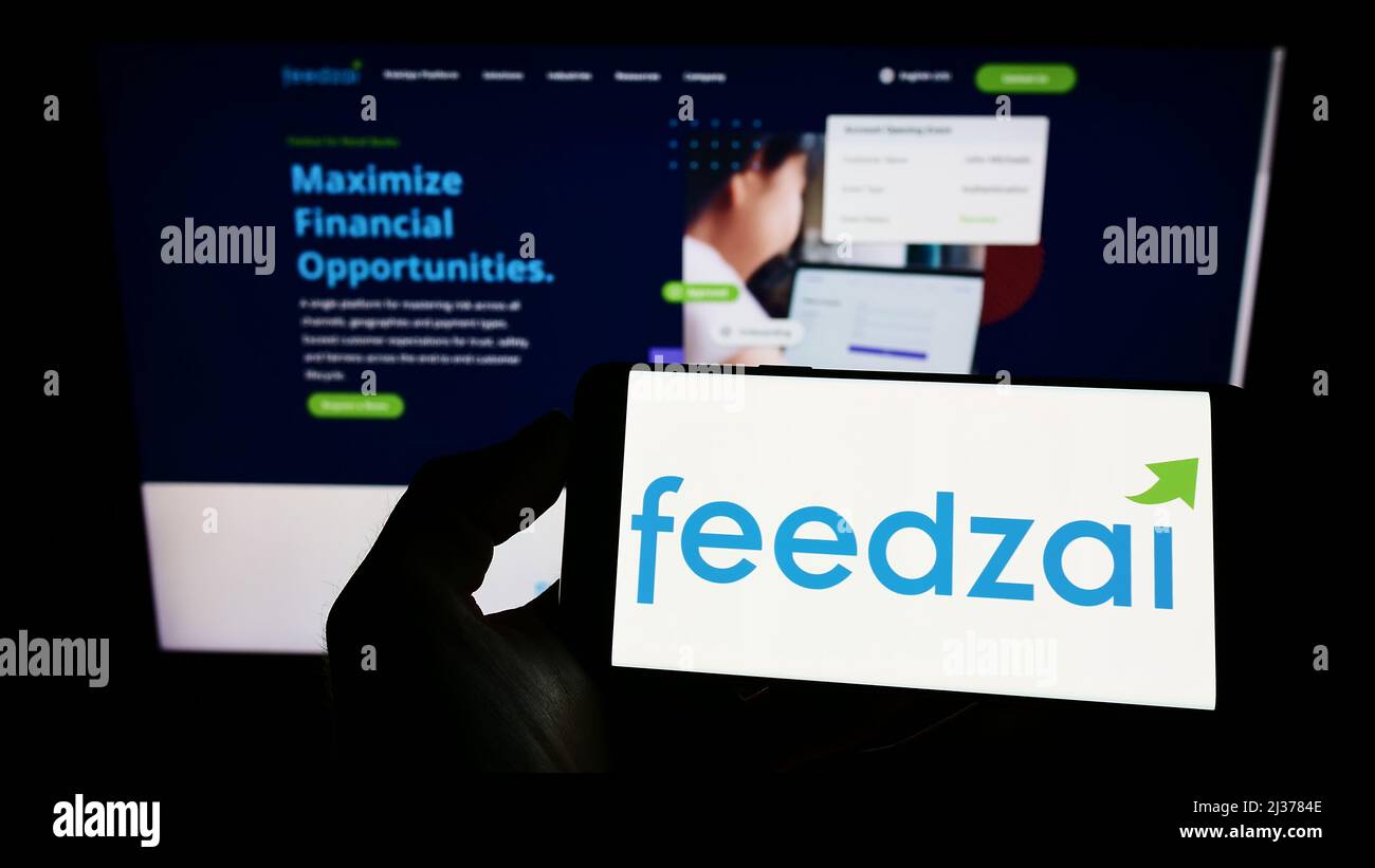 Person holding cellphone with logo of Portuguese risk management company Feedzai on screen in front of business webpage. Focus on phone display. Stock Photo