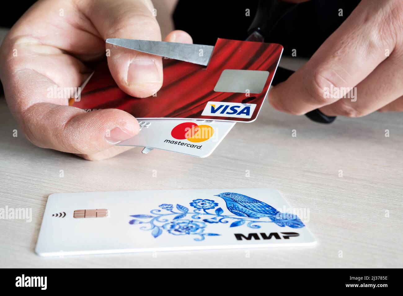 April 2, 2022. Barnaul. Russia: a man cuts bank credit cards of the type and mastercard with scissors. Destruction of plastic cards after the expirati Stock Photo