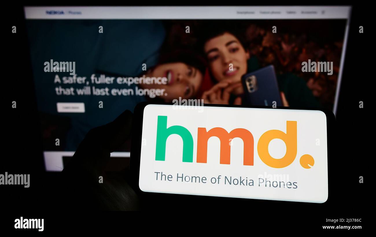 Person holding mobile phone with logo of Finnish electronics company HMD Global Oy on screen in front of business web page. Focus on phone display. Stock Photo