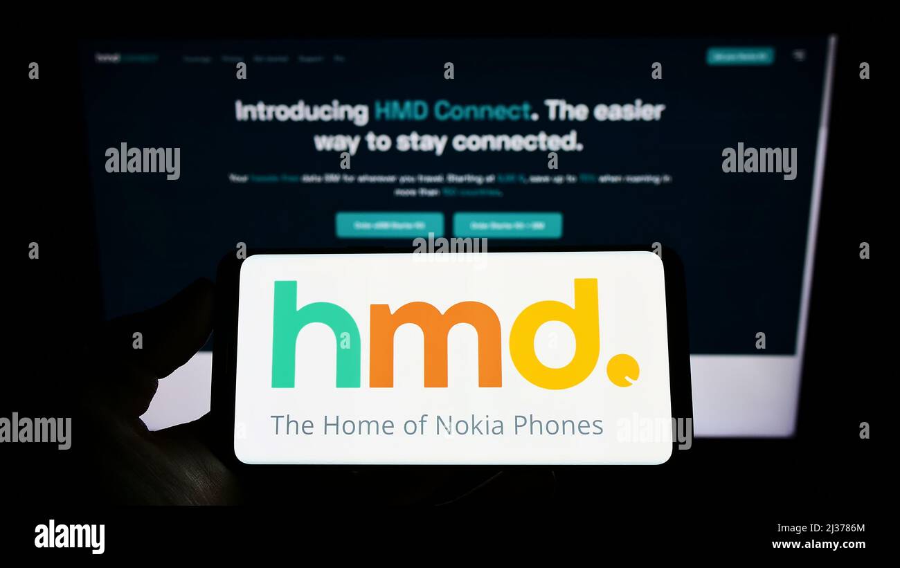 Person holding cellphone with logo of Finnish electronics company HMD Global Oy on screen in front of business webpage. Focus on phone display. Stock Photo