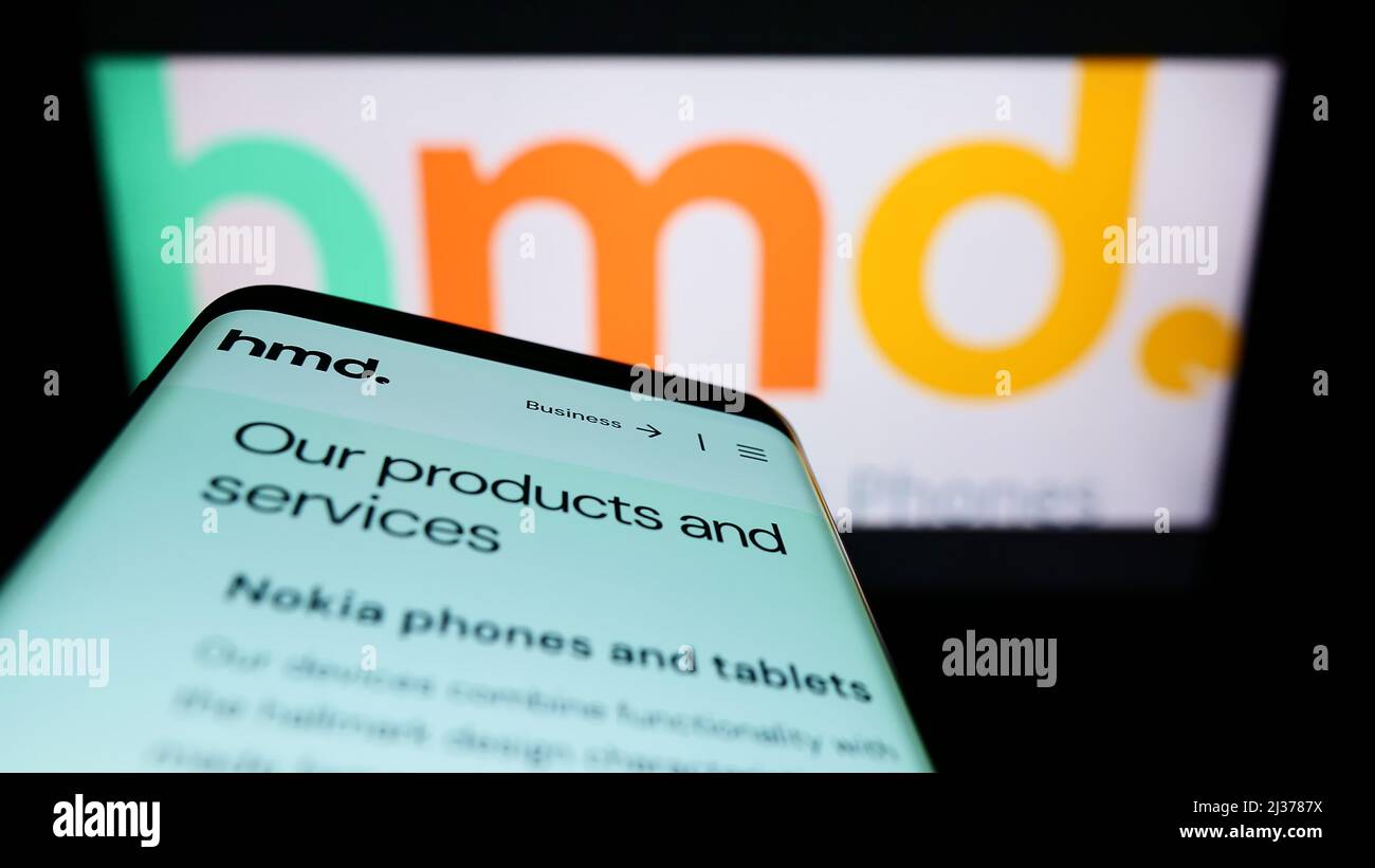 Mobile phone with website of Finnish electronics company HMD Global Oy on screen in front of business logo. Focus on top-left of phone display. Stock Photo