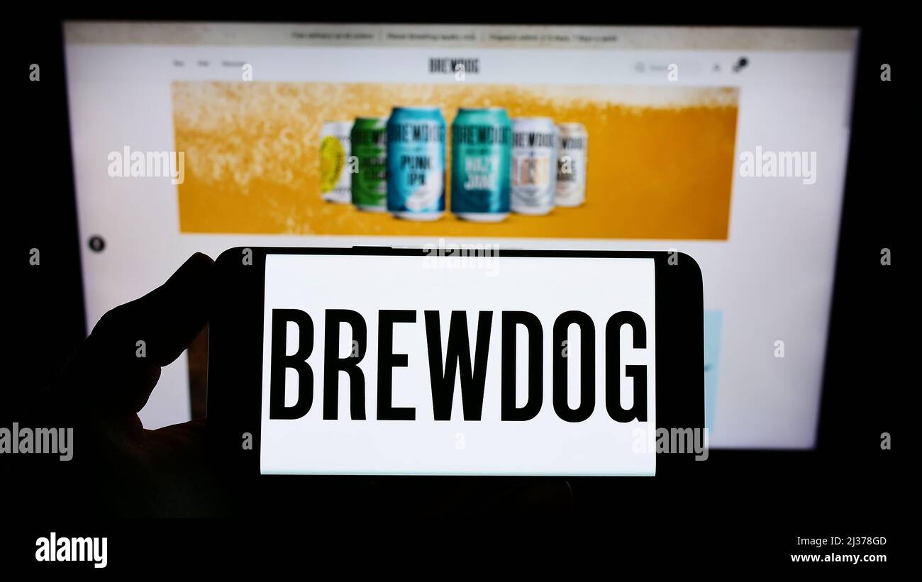 Person holding smartphone with logo of British brewery company BrewDog plc on screen in front of website. Focus on phone display. Stock Photo