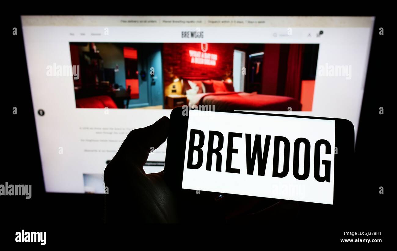 Person holding cellphone with logo of British brewery company BrewDog plc on screen in front of business webpage. Focus on phone display. Stock Photo