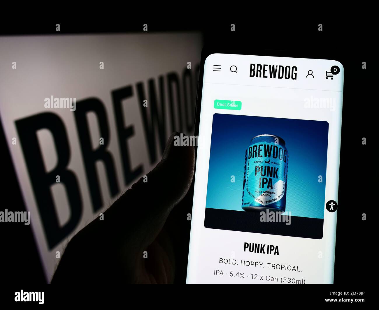 Person holding smartphone with website of British brewery company BrewDog plc on screen in front of logo. Focus on top-left of phone display. Stock Photo