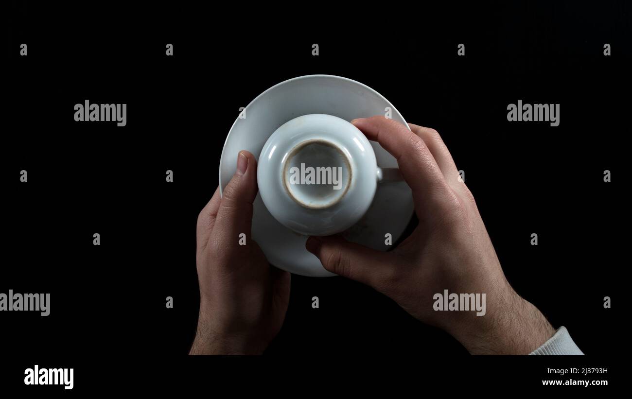 Upside down white coffee mug, fortune-telling, male hands , isolated on black background, top view Stock Photo