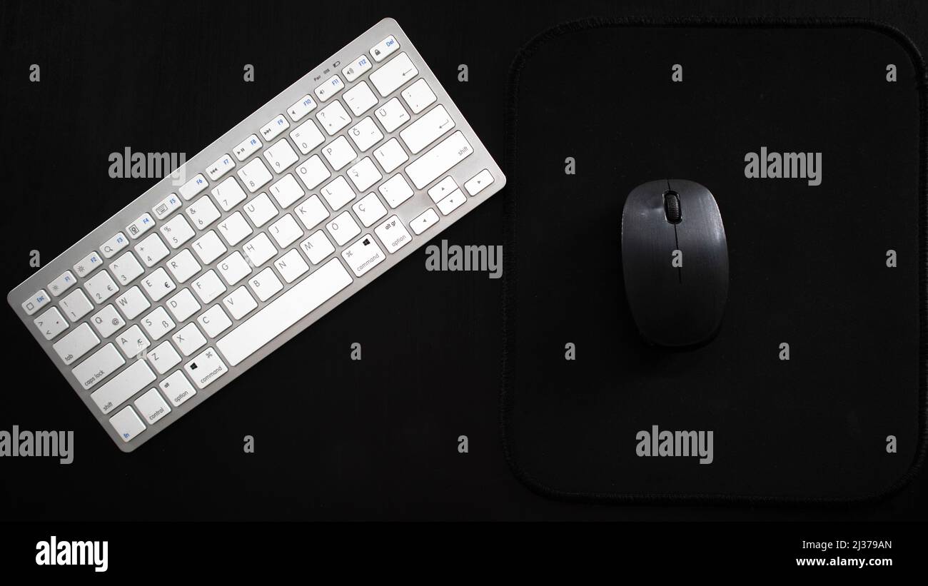 White wireless keyboard and black mouse on desk, isolated on black background, top view Stock Photo