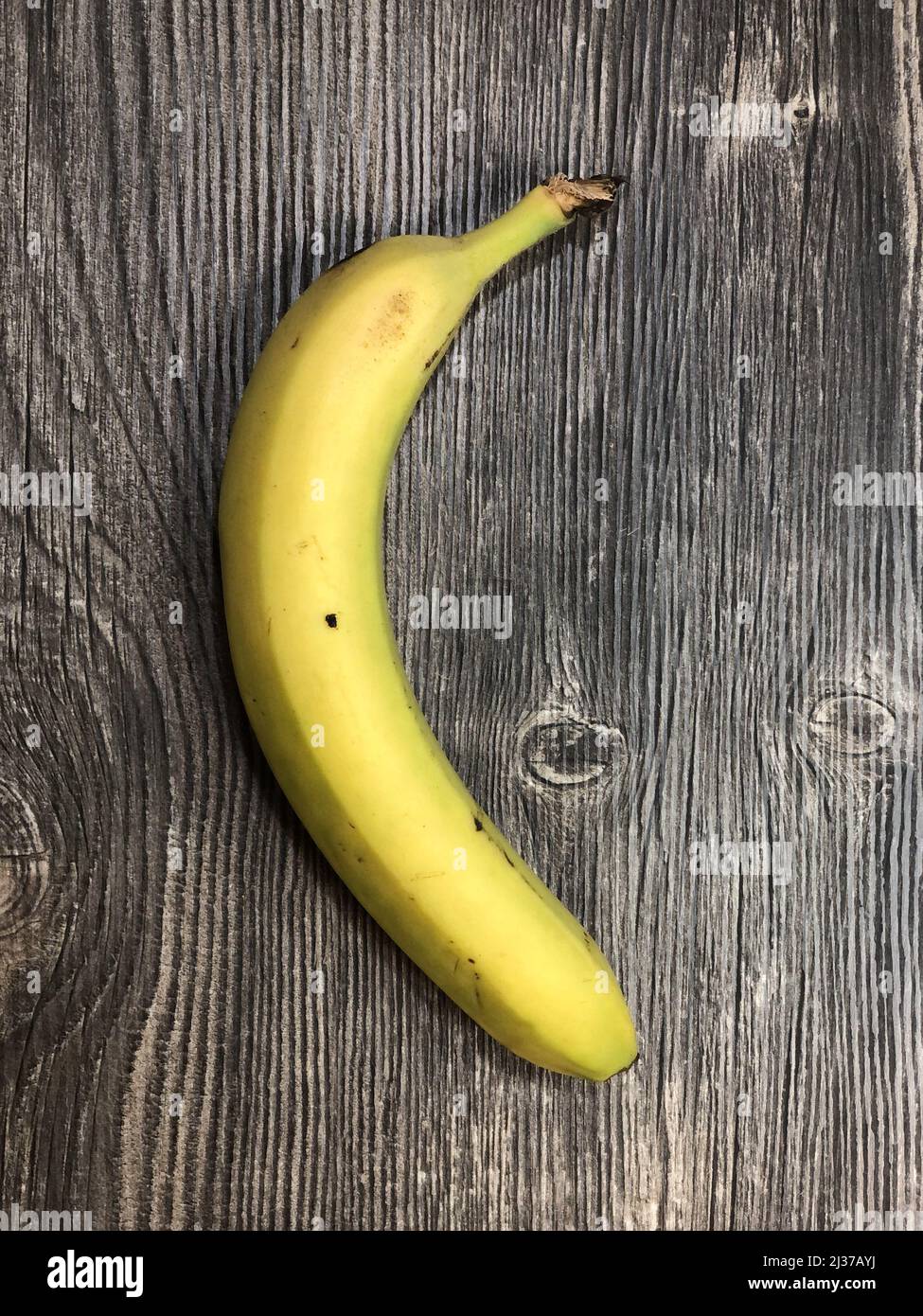 The yellow banana lying on the table with wooden texture. Close up