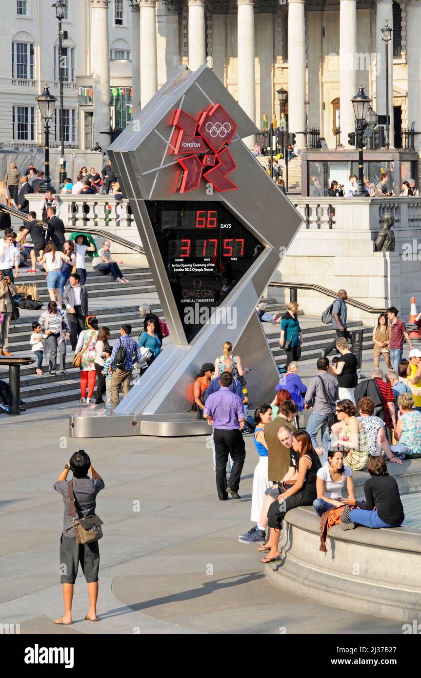 People including tourists around the Omega countdown clock in Trafalgar Square counting for opening ceremony of London 2012  Olympic Games England UK Stock Photo