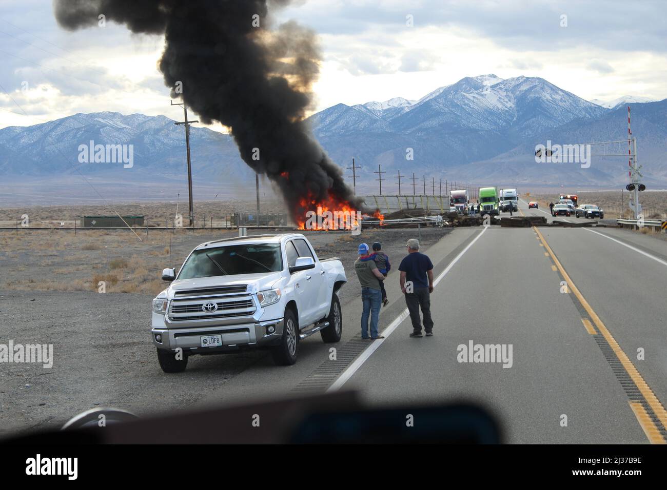 Road blocked by railroad ties and semitruck on fire on railroad tracks