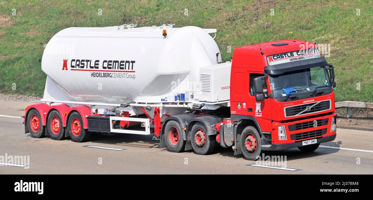 Side & front view white Heidelberg Castle Cement in bulk powder delivery tanker trailer behind red hgv lorry truck & driver travelling on UK motorway Stock Photo