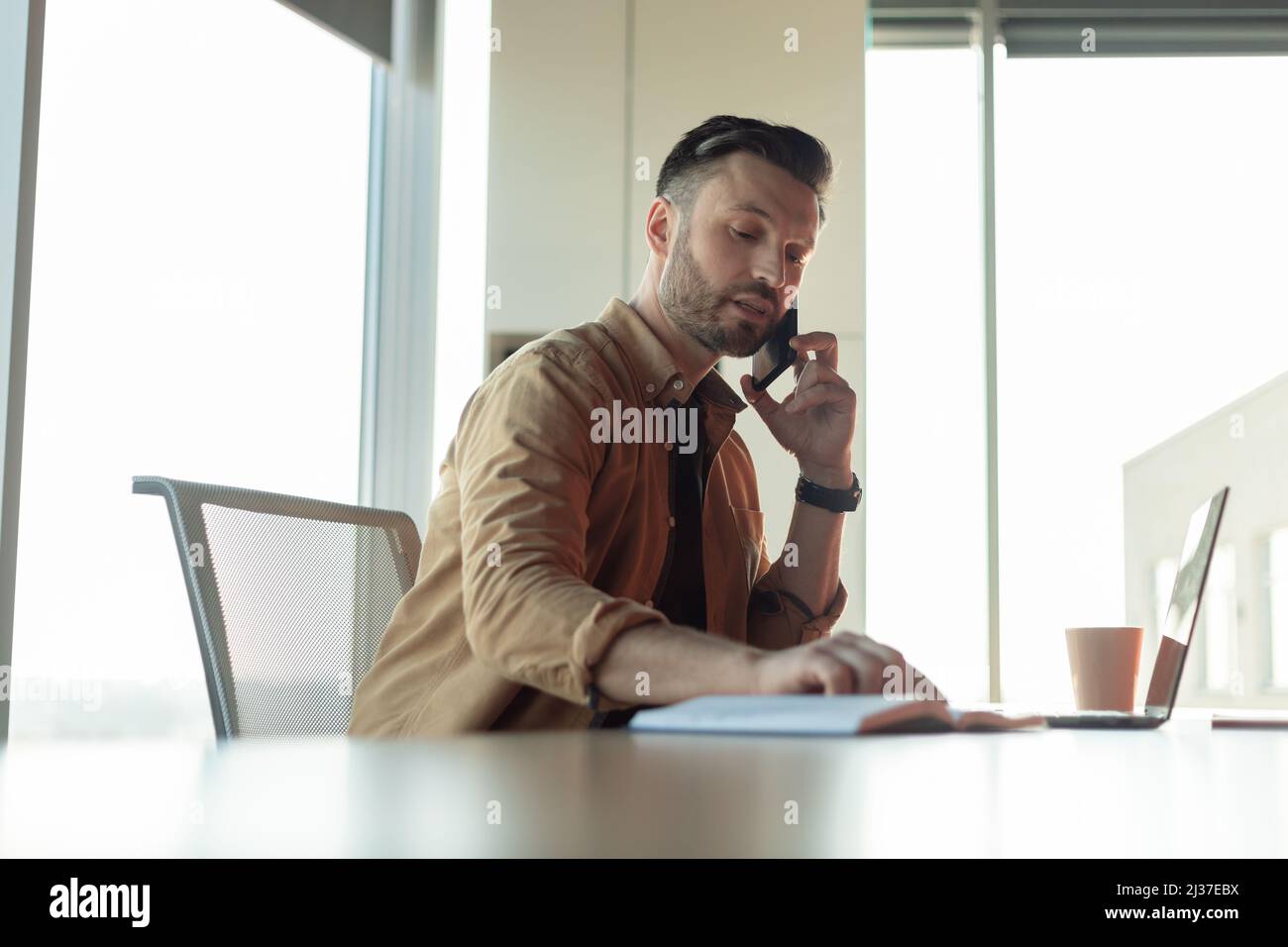 Businessman Talking On Phone Taking Notes Working Sitting At Workplace Stock Photo