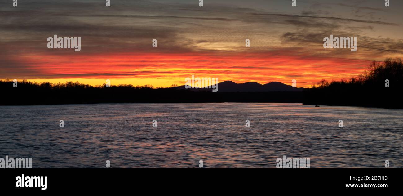 Mountain Motajica silhouette and Sava river at dusk with vivid orange clouds, calm panorama landscape at end of the day Stock Photo