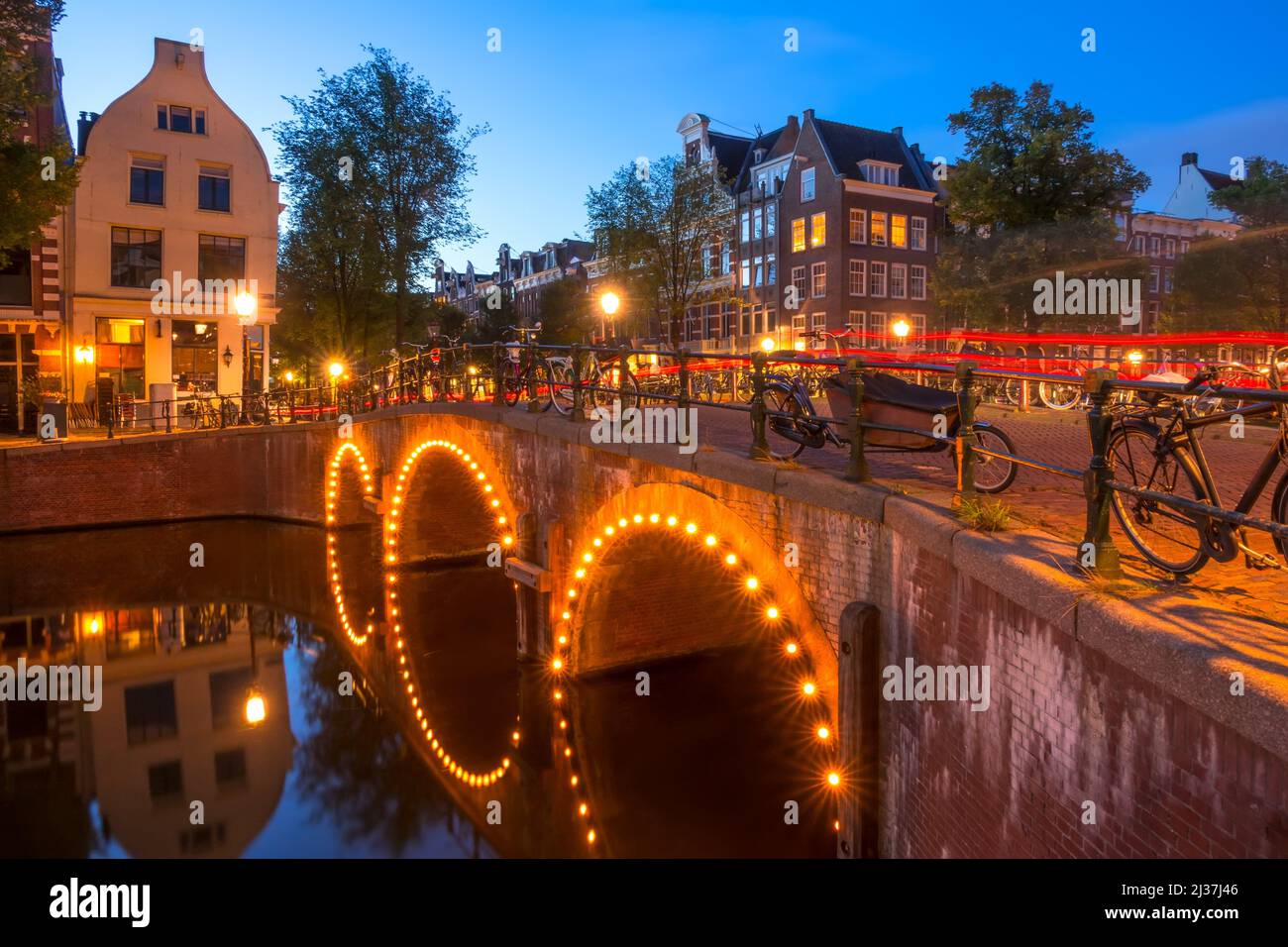 Netherlands. Stone bridge with three arches on the Amsterdam Canal. Lots of parked bikes. End of the night. Stock Photo