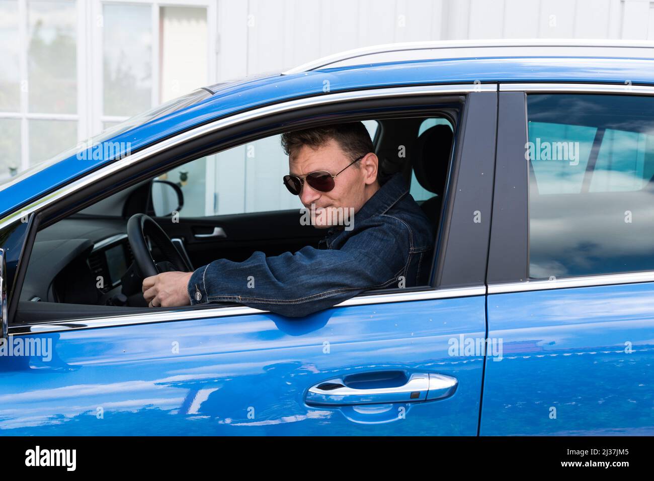 Oregrund, Uppland - Sweden - 30 07 2019- Fourty year old fashionable man with sunglasses posing in his blue Kia Sportage car. Stock Photo