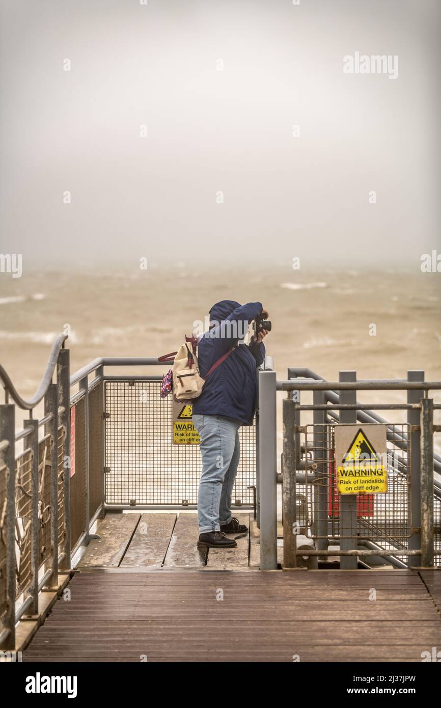 East Sussex, UK. 6th april 2022, Strong winds and heavy rain dampen the Easter school holidays as a tourist takes a photo of the Seven Sisters in bad weather at  Birling Gap ,East Sussex, UK. Stock Photo