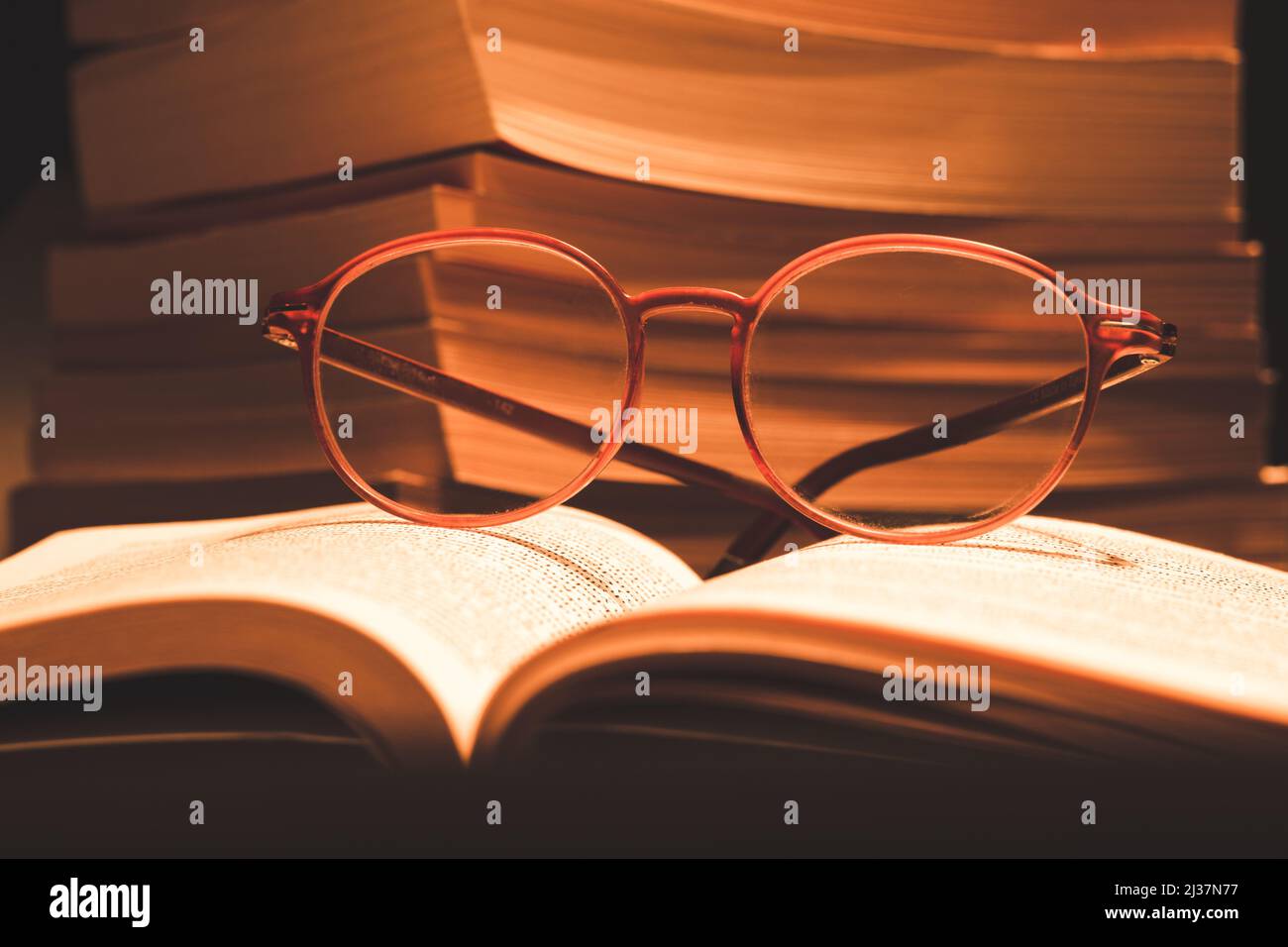 Glasses on book in selective focus. Books stacked out of focus. Book reading, education, rest, knowledge concept vintage background. Stock Photo