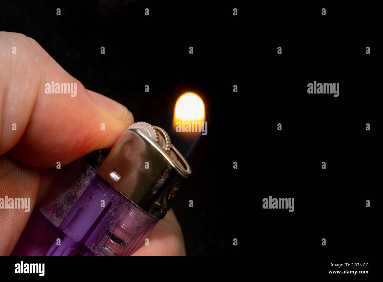 Lighting a lighter close-up. Transparent purple plastic gas chamber lighter lit by a hand. Stock Photo