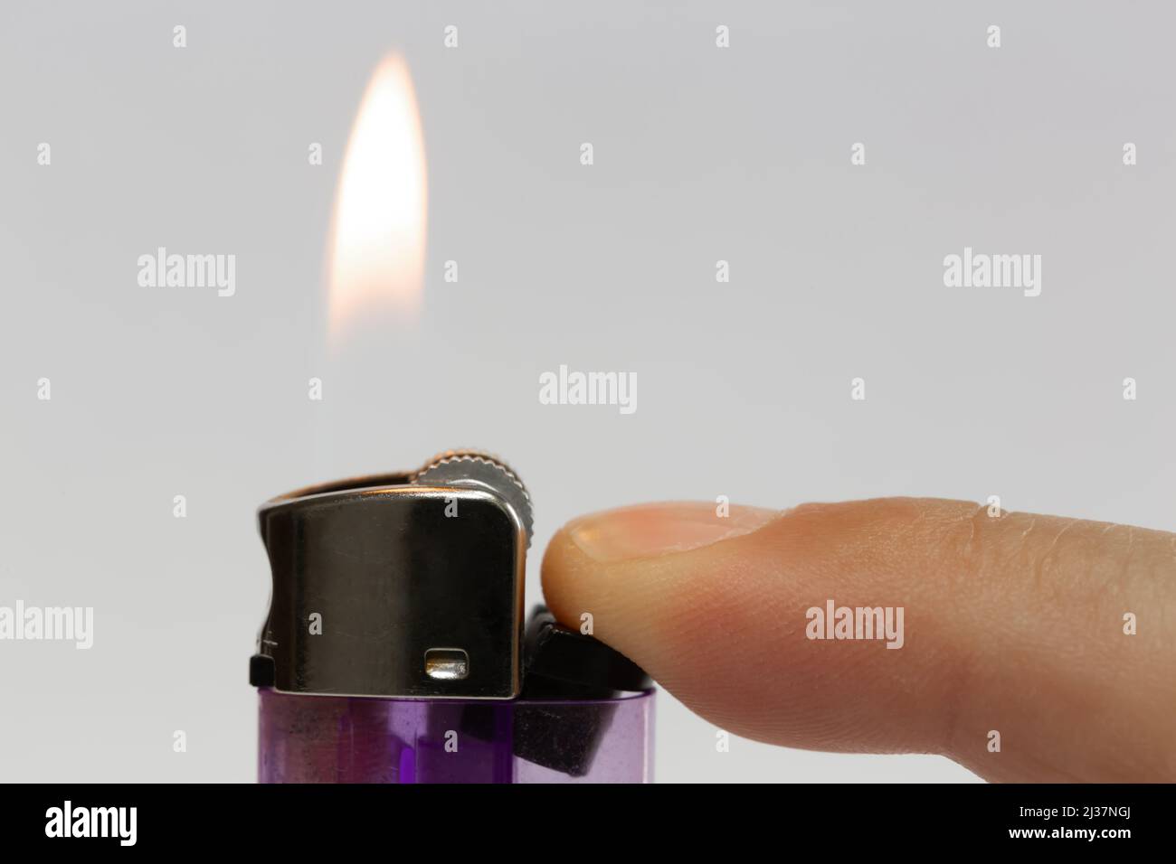 Close-up lighter burn isolated on white background. Transparent purple plastic gas chamber lighter lit by a finger. Stock Photo