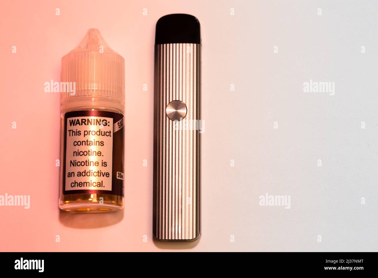 Electronic cigarette liquid bottle and pod mod electronic cigarette. The plastic bottle reads 'Warning: This product contains nicotine. Nicotine is an... Stock Photo