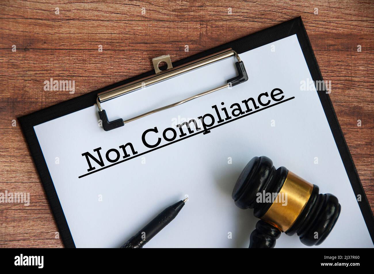 Non compliance text on paper with gavel, pen and wooden background. Stock Photo