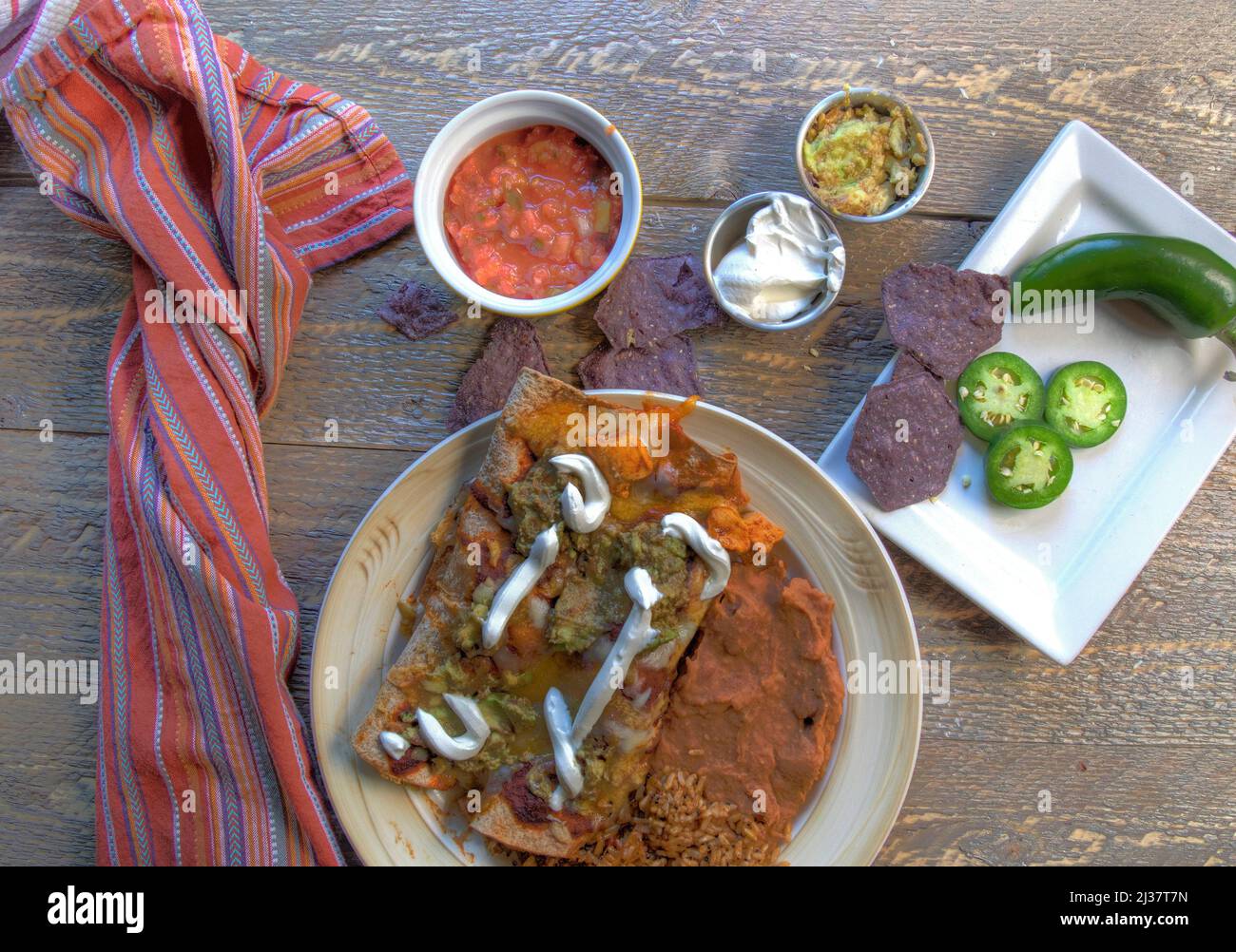 Mexican enchilada dinner with chips salsa and jalapenos on natural wood table top view. Stock Photo