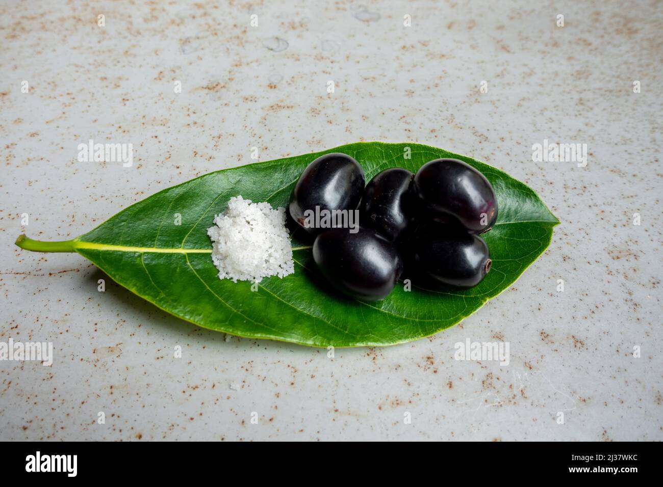 Spicy mixed salt with some black java plum fruit in the green leaves. A way to eat ripe cesium camini fruit by hand. 4k closeup video. Stock Photo