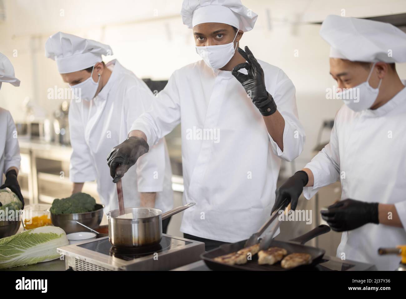 Multiracial team of chef cooks in white uniform cooking together in the